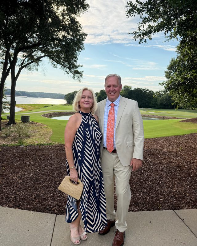 Scott Allison and a woman in evening wear on a lawn beside a lake