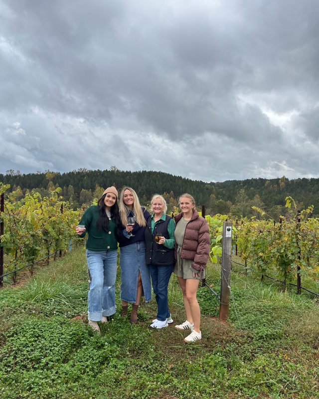 Four women standing between rows of vines at a vineyard