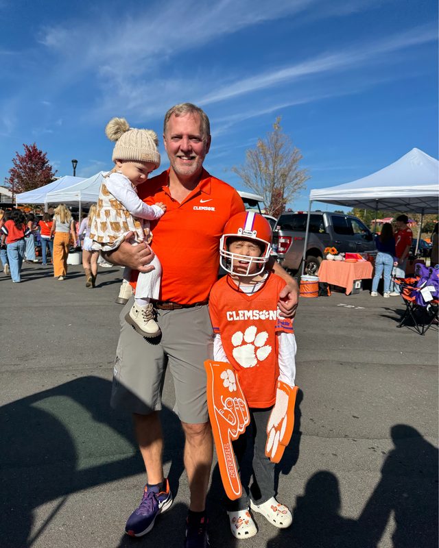 Scott Allison at a tailgate holding a toddler, with a child in a Clemson jersey beside him