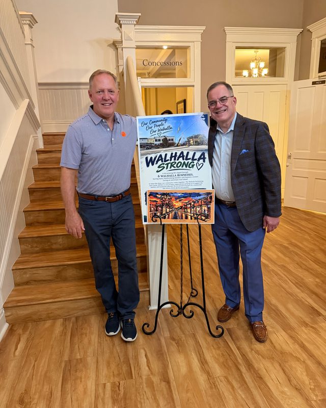 Scott Allison and another man beside a Walhalla Strong poster on an easel at an indoor event